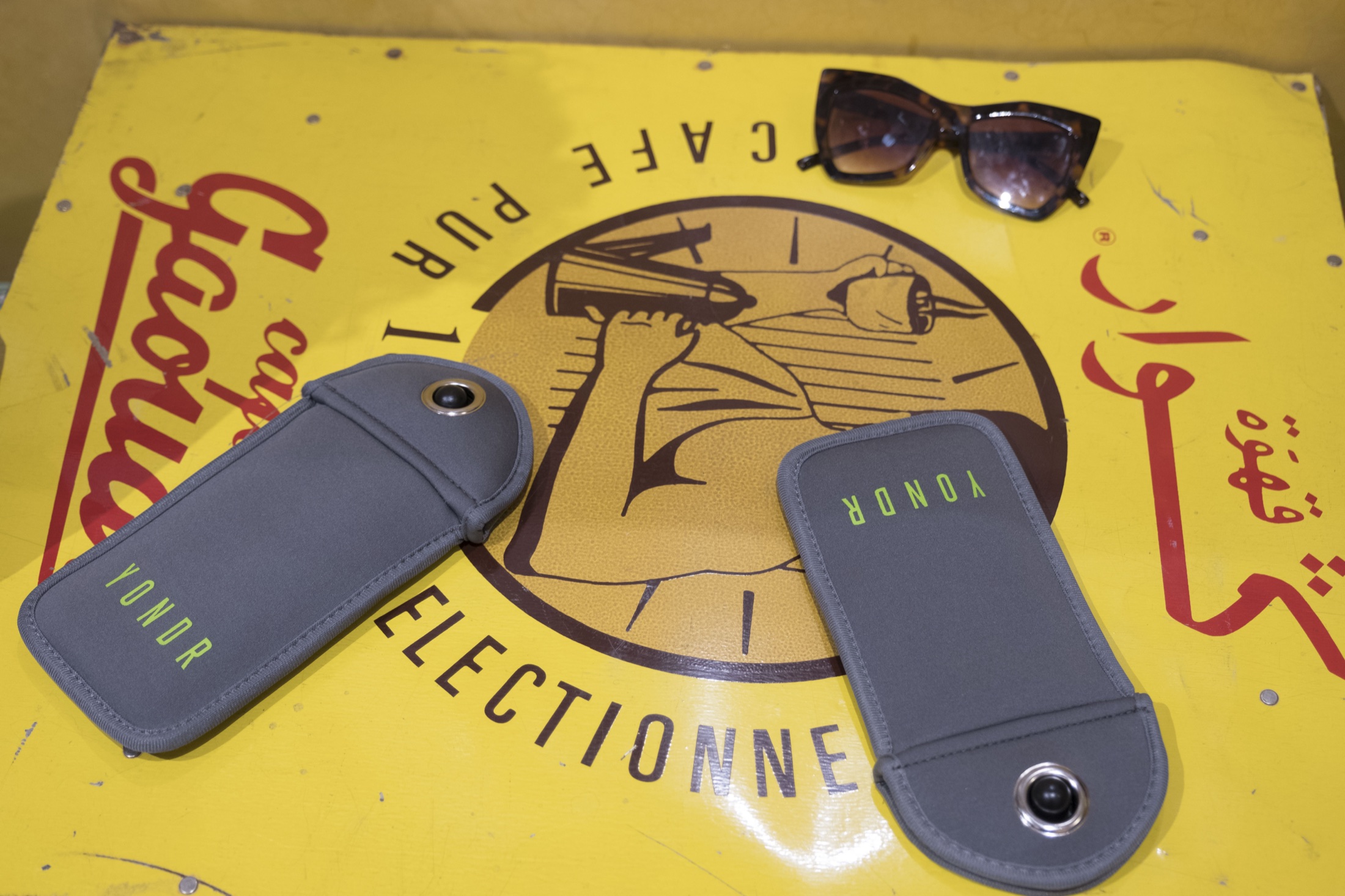 Yondr pouches and sunglasses on a yellow table at Cafe du Livre
